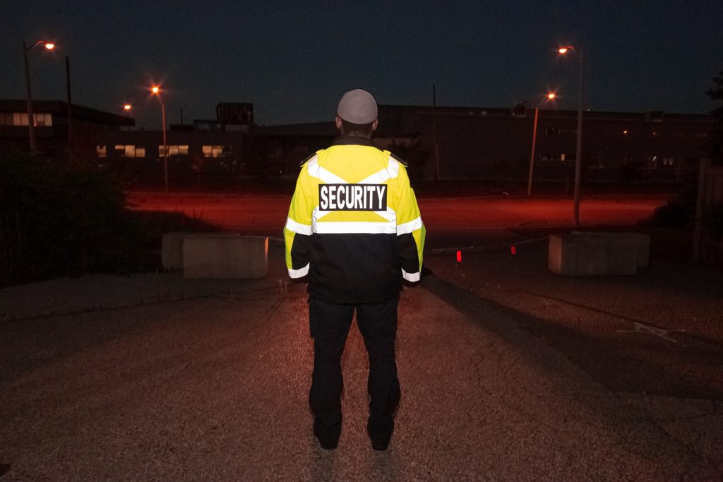 man in yellow and black jacket standing on sidewalk during night time